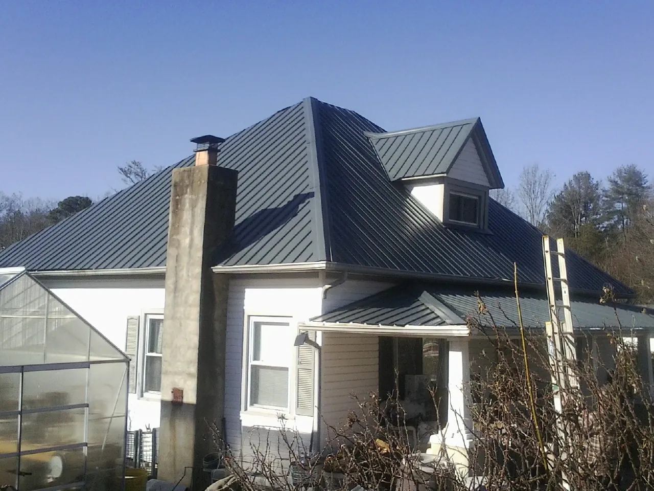Dark blue standing seam metal roof on a white farmhouse with dormer in Guymon