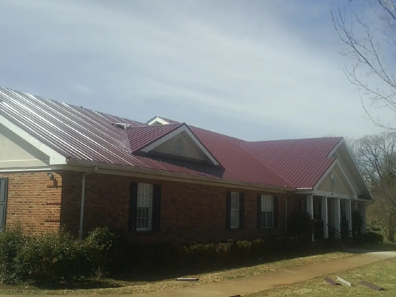 Red metal roof with gabled entries on a long brick building, from a Hail Damage Roof Repair job in Guymon