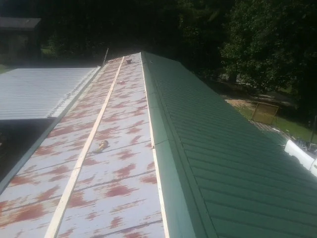 Old rusted panels beside newly installed green metal roofing — Wind Damage Roof Repair by Roofing Brothers in Guymon