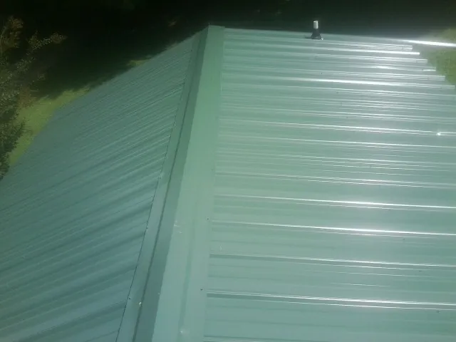 New green metal panels meeting at the ridge of a roof — Flat Roof Repair work by our crew in Guymon