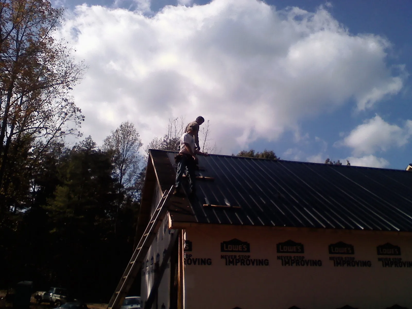 Roofer fastening dark metal panels high against a cloudy sky, from a Roof Inspection job in Guymon
